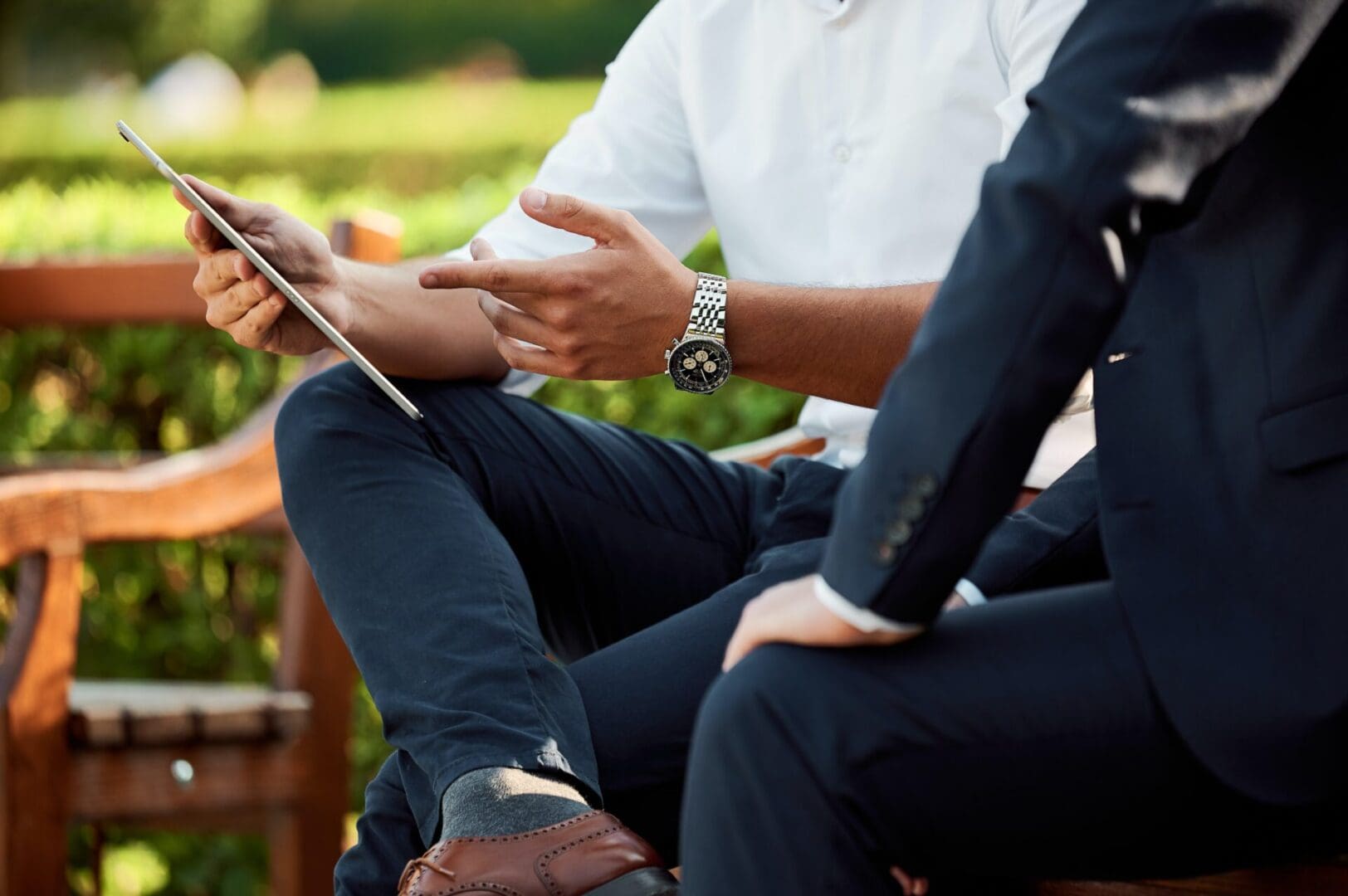 Two people sitting on a bench with one holding an ipad.